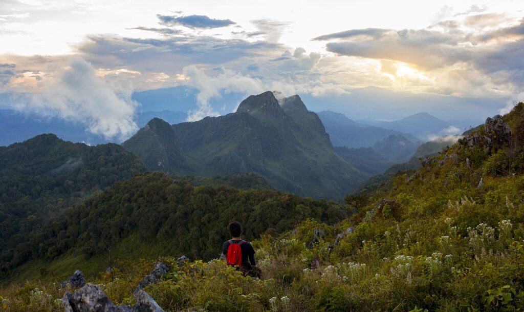 Randonneur avec un sac à dos rouge admirant la vue panoramique sur les sommets du Doi Chiang Dao au coucher du soleil.