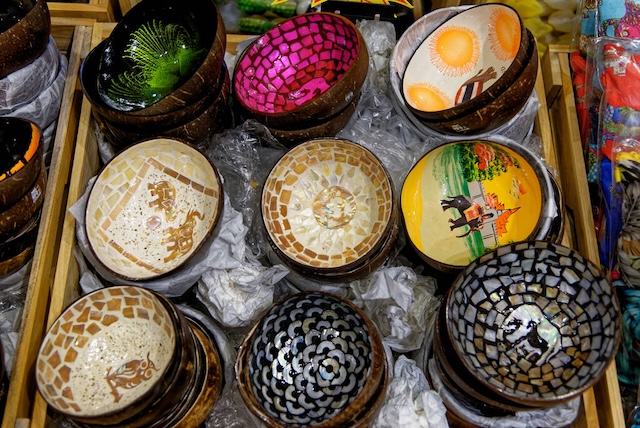 Plusieurs bols en coque de noix de coco décorés avec des mosaïques et peintures colorées sur un étal de marché en Thaïlande.