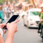 Femme découvrant son compte bancaire bloqué au Vietnam sur son smartphone dans une rue animée.