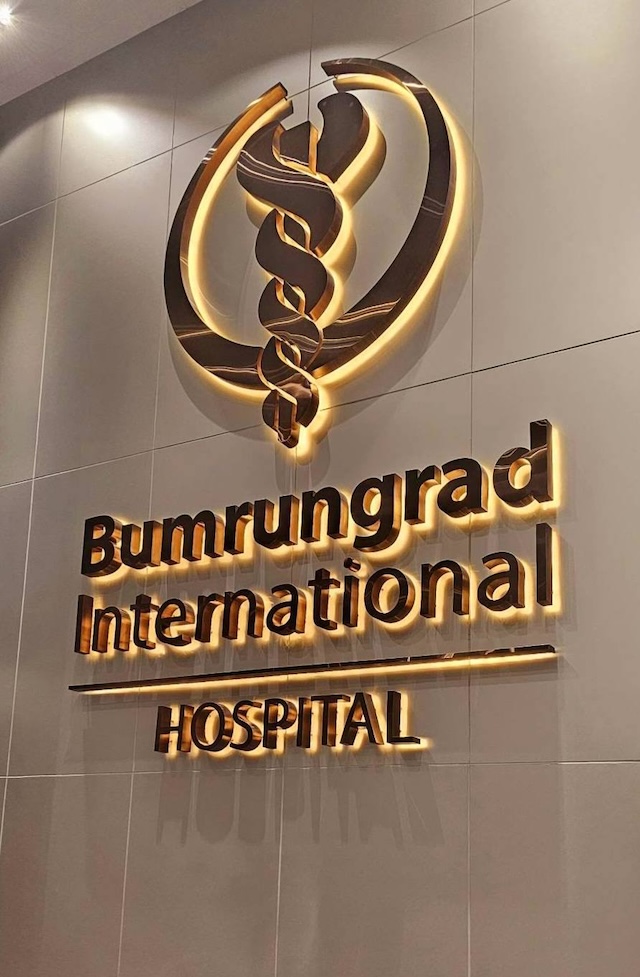 Logo rétro-éclairé en bronze de l'hôpital international Bumrungrad sur un mur carrelé.