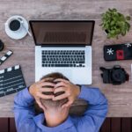 Un nomade digital se tient la tête avec frustration devant son ordinateur, illustrant les difficultés pour ouvrir un compte bancaire en Thaïlande avec un visa DTV.