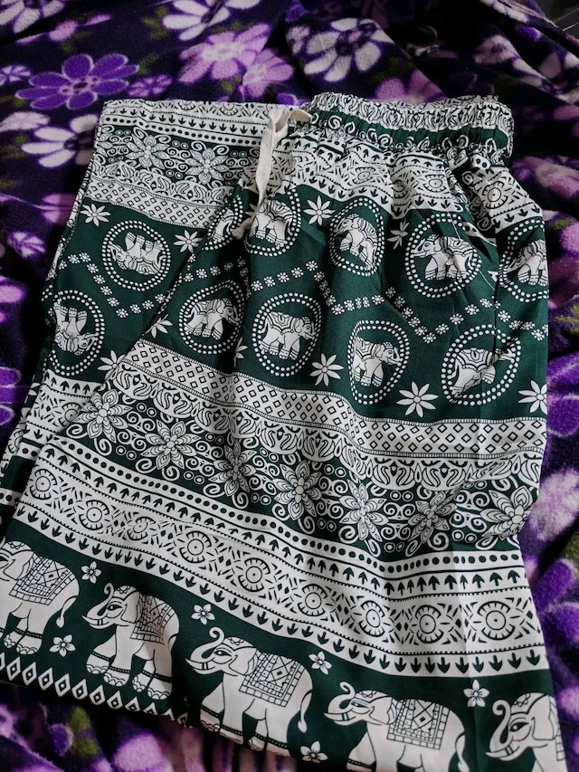 Gros plan sur un pantalon éléphant traditionnel thaïlandais de couleur verte avec des motifs d'éléphants et floraux blancs, plié sur une couverture.