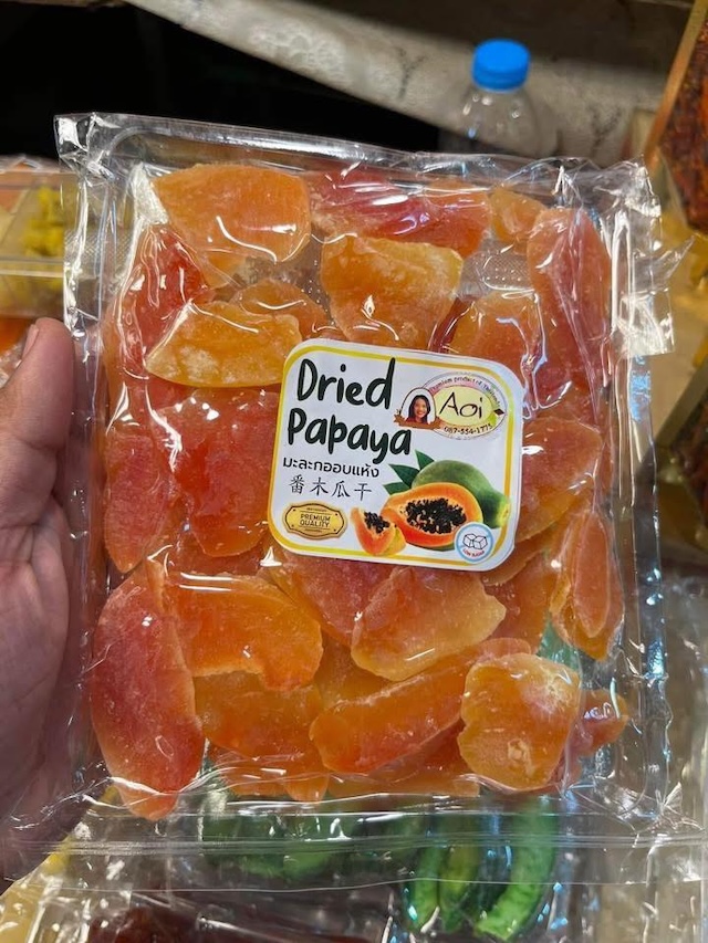 Sachet transparent de papaye séchée de la marque Aoi, tenu dans la main sur un marché en Thaïlande.