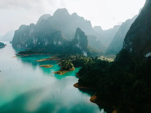 Vue aérienne du lac Cheow Lan aux eaux turquoise, entouré par les montagnes karstiques et la jungle dense du Parc National de Khao Sok en Thaïlande.
