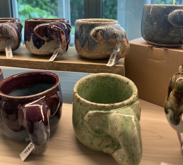 Plusieurs tasses en céramique artisanale avec une anse en forme de tête d'éléphant, présentées sur un étal de marché en Thaïlande.