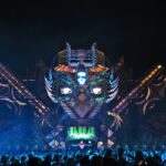 Vue nocturne d'une impressionnante scène principale de Tomorrowland, avec un décor en forme de créature fantastique illuminée et une large foule de festivaliers.