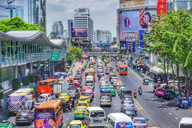 Vue d'une avenue de Bangkok avec un trafic très dense de voitures, bus, taxis colorés et scooters, illustrant les conditions de circulation difficiles.