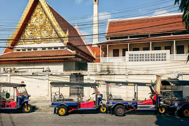 Plusieurs tuk-tuks colorés garés devant un temple thaïlandais, illustrant le contexte typique d'une arnaque touristique à Bangkok.