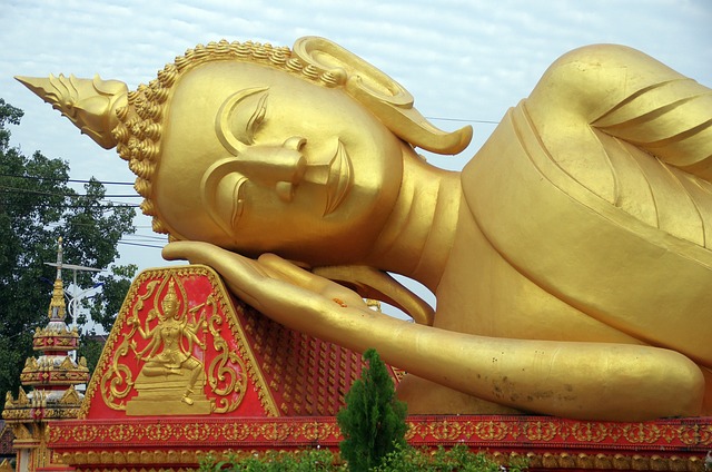 Grande statue dorée du Bouddha couché au Buddha Park (Xieng Khuan) à Vientiane, Laos, avec un ciel nuageux en arrière-plan.