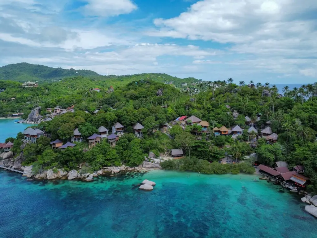 Vue aérienne d'une île tropicale dans le Golfe de Thaïlande avec bungalows sur la colline et mer turquoise, illustrant le choix entre Koh Samui, Koh Phangan et Koh Tao.
