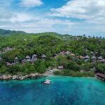 Vue aérienne d'une île tropicale dans le Golfe de Thaïlande avec bungalows sur la colline et mer turquoise, illustrant le choix entre Koh Samui, Koh Phangan et Koh Tao.