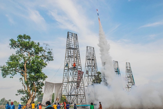 Une fusée artisanale décolle d'une haute tour de lancement en métal, laissant un épais panache de fumée, lors du festival Bun Bang Fai en Isan, Thaïlande.