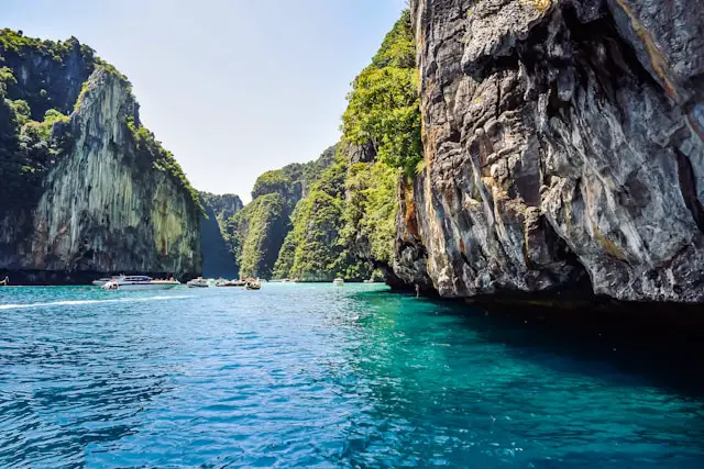 Mer turquoise claire et falaises karstiques abruptes à Krabi, avec des bateaux, illustrant la nature sauvage et les excursions en mer.