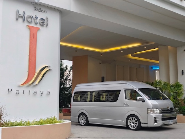 Minivan argenté de type Toyota Commuter garé devant l'entrée de l'hôtel J à Pattaya, illustrant une option de transport privé.