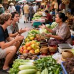Deux touristes en train de négocier avec une vendeuse souriante sur un marché de fruits et légumes en Thaïlande.