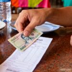 Main d'un voyageur laissant un billet de 100 bahts en pourboire sur une addition dans un restaurant en Thaïlande.