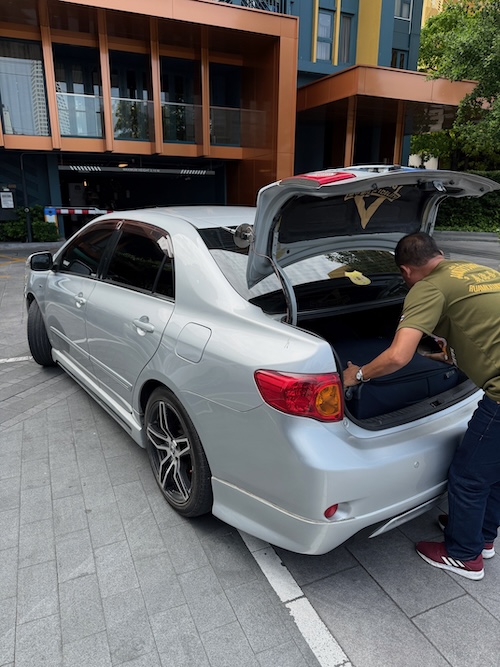 Chauffeur de VTC plaçant une valise dans le coffre d'une voiture argentée devant un condo, illustrant le transport privé avec bagages.
