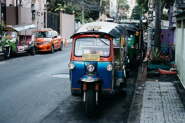 Tuk-tuks colorés garés dans une rue typique de Bangkok, en Thaïlande, illustrant les transports locaux où la négociation et le pourboire sont des sujets importants.