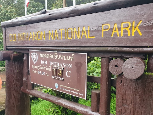 Panneau en bois « Doi Inthanon National Park » avec affichage de la température à 13°C entouré de végétation tropicale