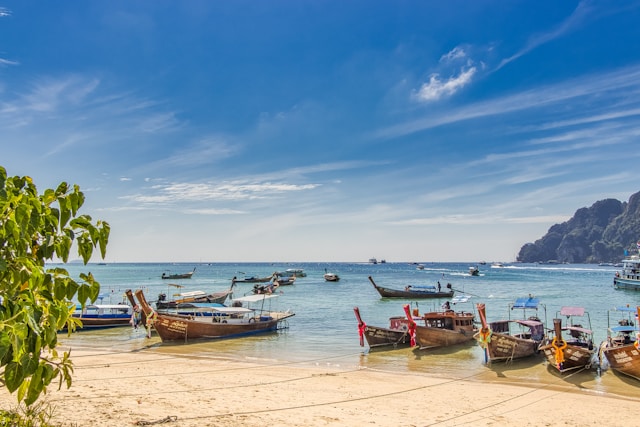 Bateaux traditionnels sur une plage du sud de la Thaïlande sous un ciel bleu éclatant, loin de la pollution du nord.