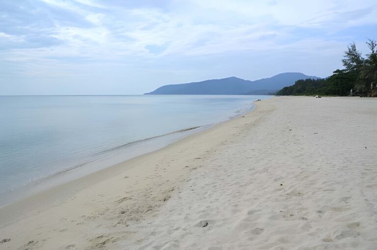 Plage de sable doré presque déserte à Nadan Beach à Khanom en Thaïlande, avec la mer calme et des montagnes en arrière-plan