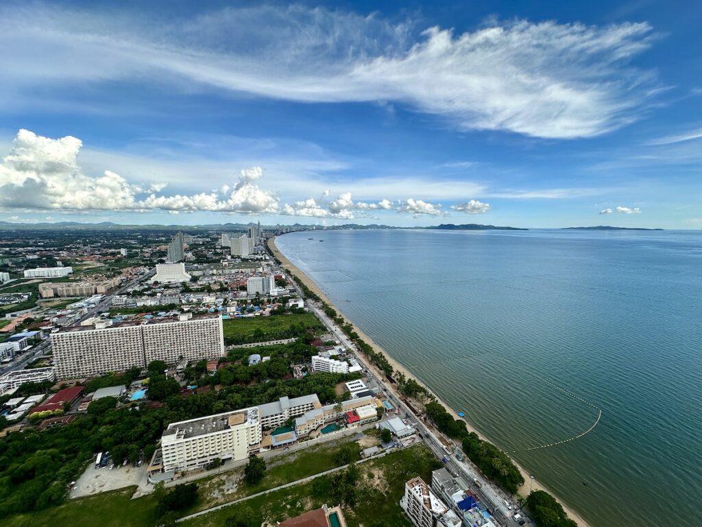 Panorama aérien de la plage de Jomtien en Thaïlande : une longue étendue de sable calme bordée d'arbres et de condos, contrastant avec l'agitation de Pattaya