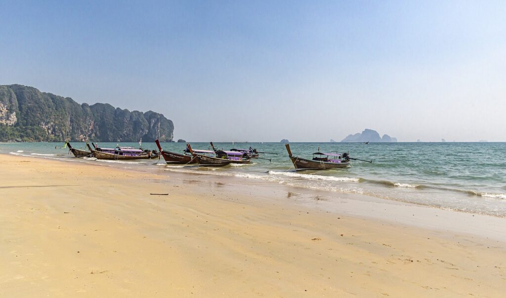Plage d’Ao Nang en Thaïlande avec bateaux long-tail et falaises karstiques
