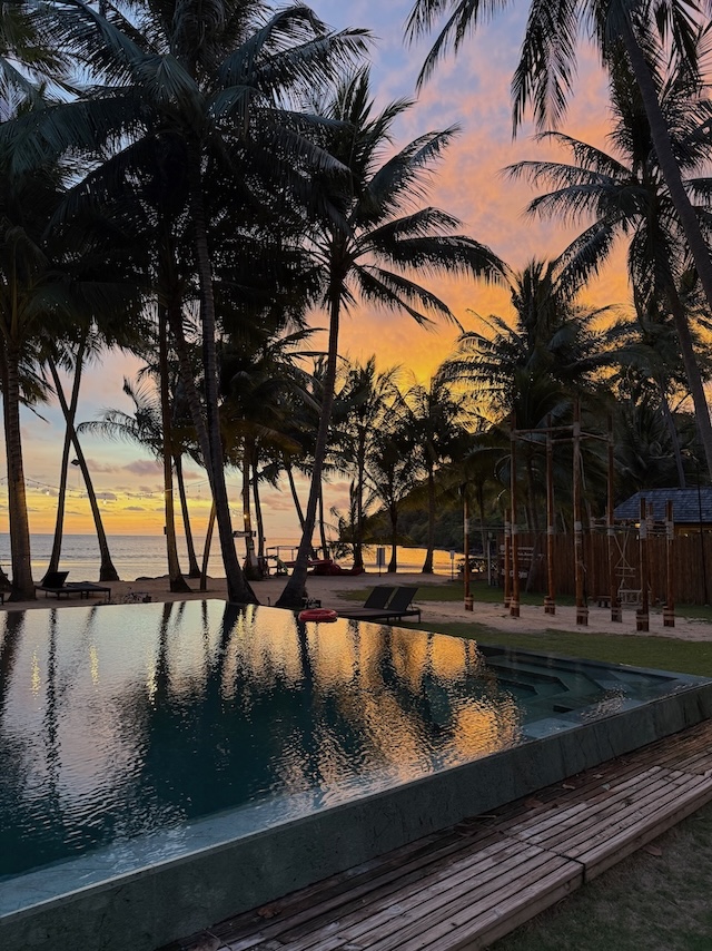 Coucher de soleil sur une plage de Koh Chang avec piscine et palmiers au premier plan
