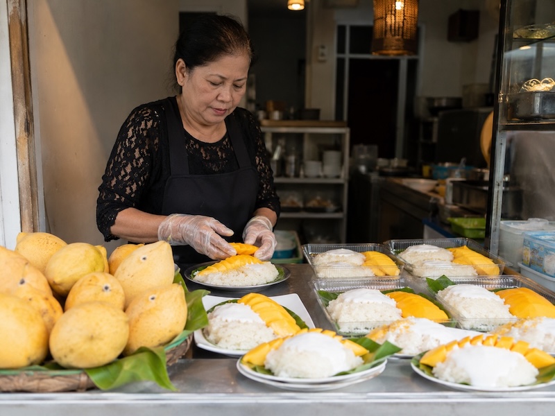 Vendeuse préparant du mango sticky rice avec mangues fraîches et riz gluant en Thaïlande