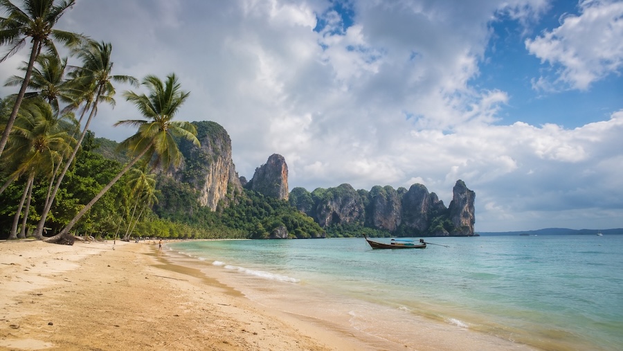 Plage de Krabi en octobre avec falaises karstiques, barque traditionnelle et ciel variable