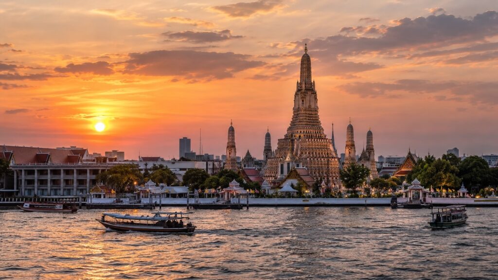 Wat Arun au coucher du soleil à Bangkok, avec des bateaux naviguant sur le fleuve Chao Phraya.