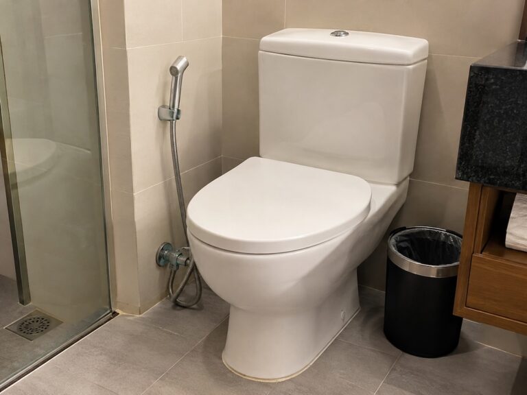 Toilettes d'un hôtel en Thaïlande avec une douchette hygiénique et une petite poubelle à côté de la cuvette.
