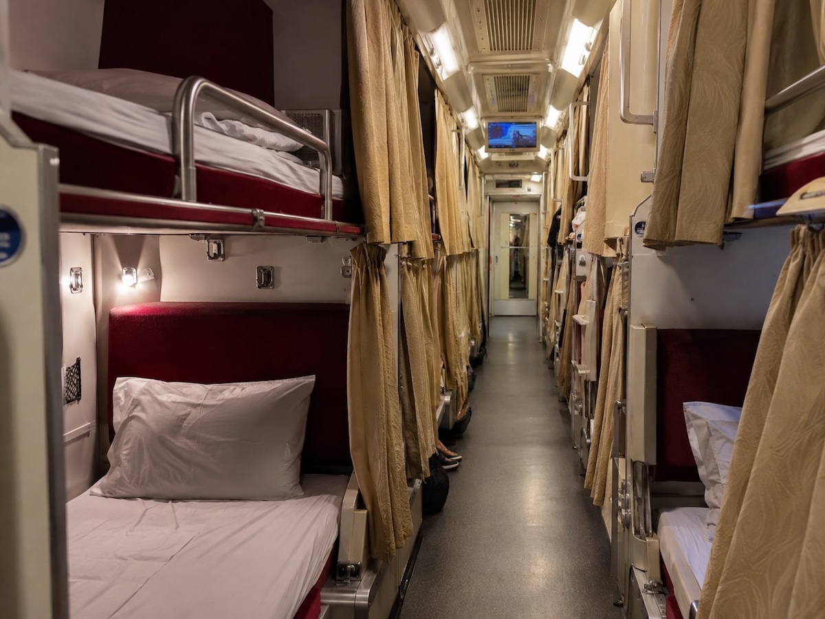 Couchettes superposées avec rideaux et couloir central dans un train de nuit thaïlandais